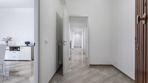 Un couloir moderne avec un plancher en bois, des murs blancs et un espace cuisine visible sur la gauche.