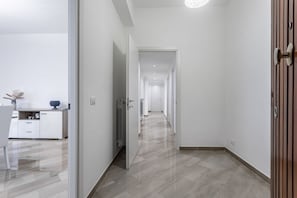 A modern hallway with a wooden floor, white walls, and a kitchen area visible to the left.