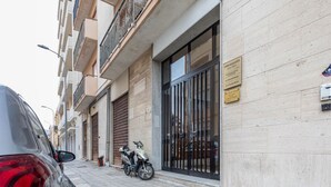 Un immeuble résidentiel avec une entrée sécurisée par un portail, un scooter garé et une voiture dans la rue.