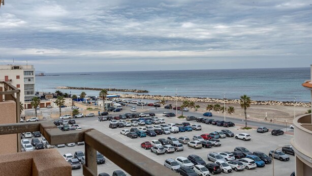 Un parking rempli de voitures, une plage et un bâtiment en arrière-plan.