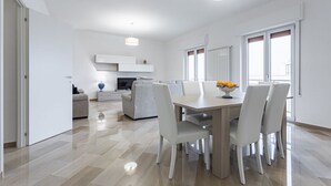Un salon moderne et bien éclairé, comprenant un coin repas, un canapé, un téléviseur et un panier de fruits posé sur la table.