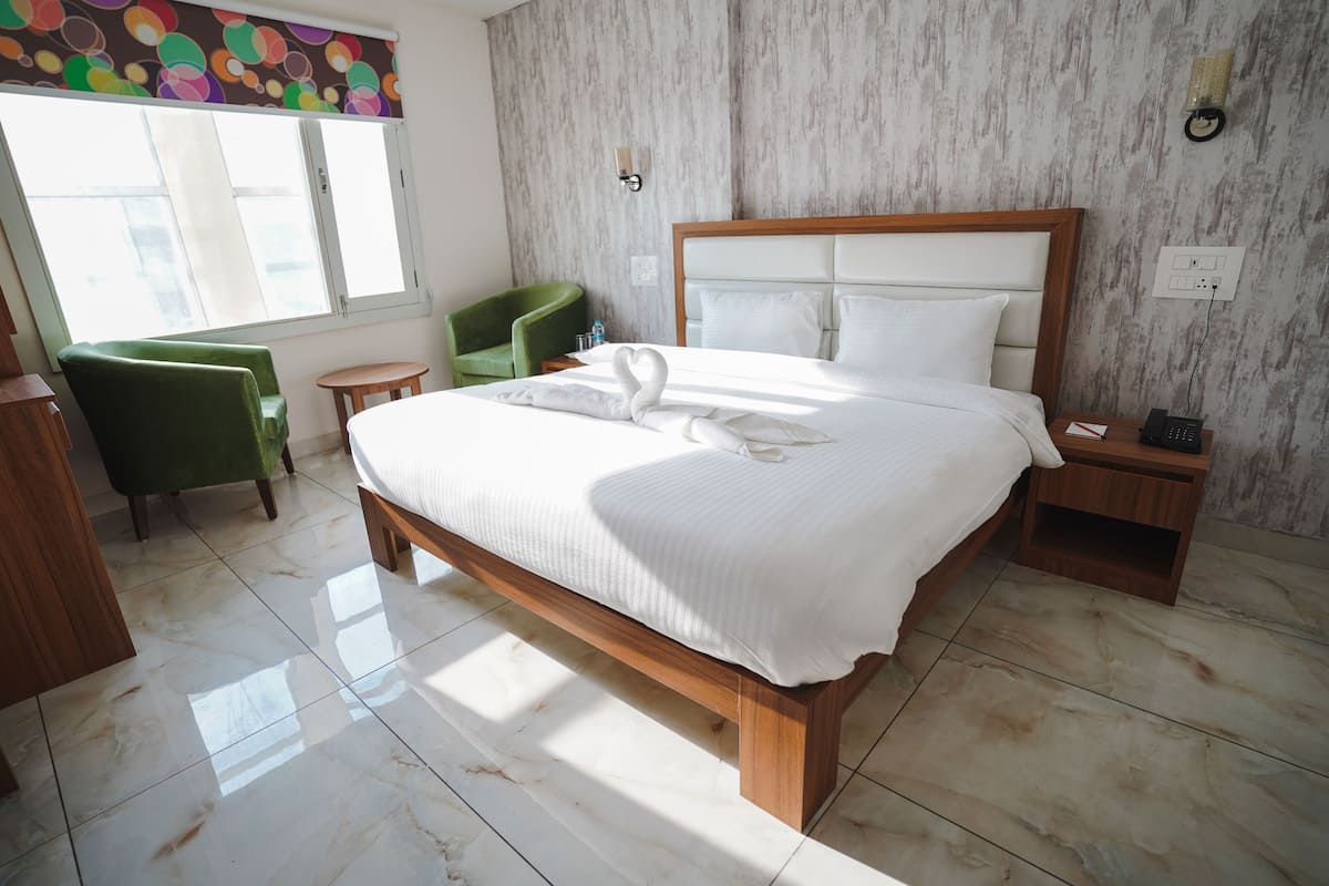 A hotel room with a large bed, a green chair, a small round table, and a window with a view.