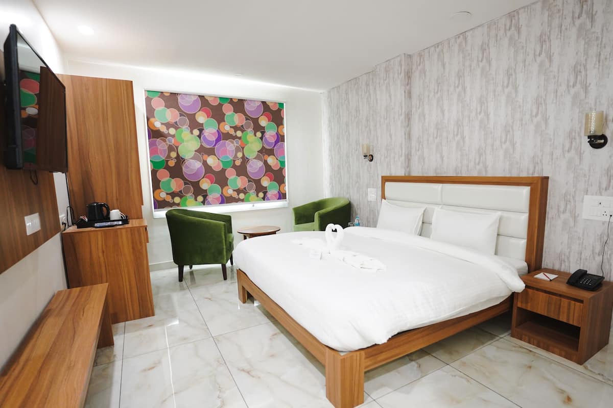 A hotel room with a wooden bed, a desk, green chairs, a TV, and a colorful abstract wall.