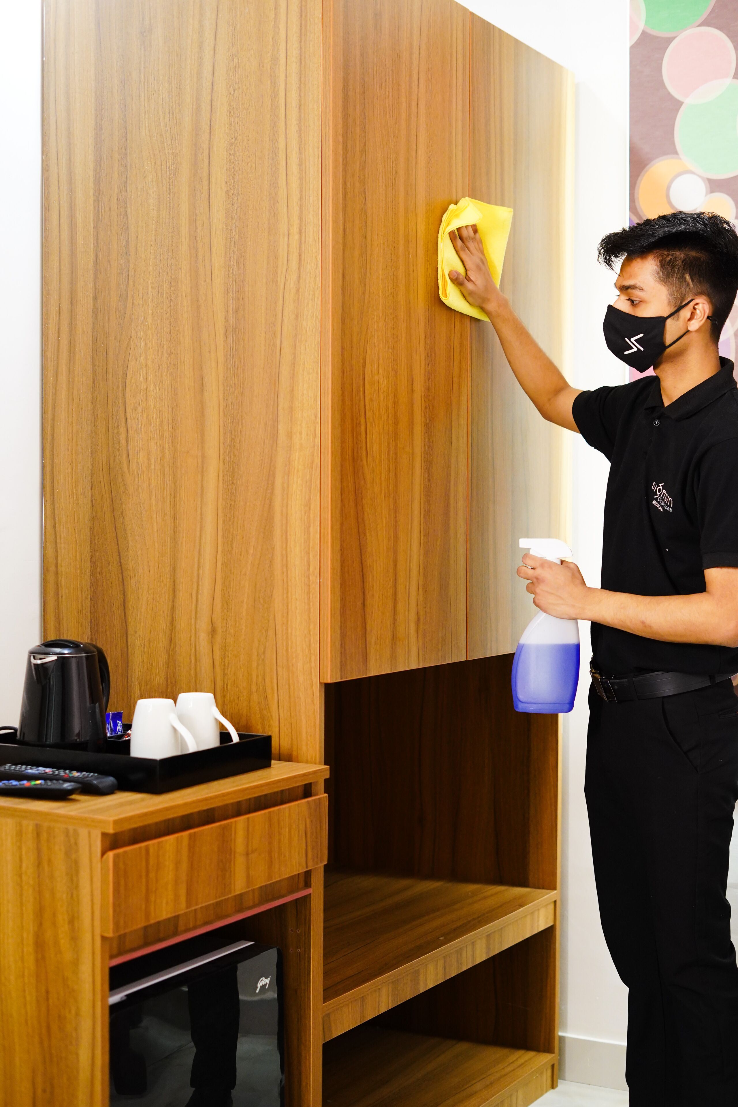 Una persona limpiando un armario de madera con un paño amarillo y un pulverizador.