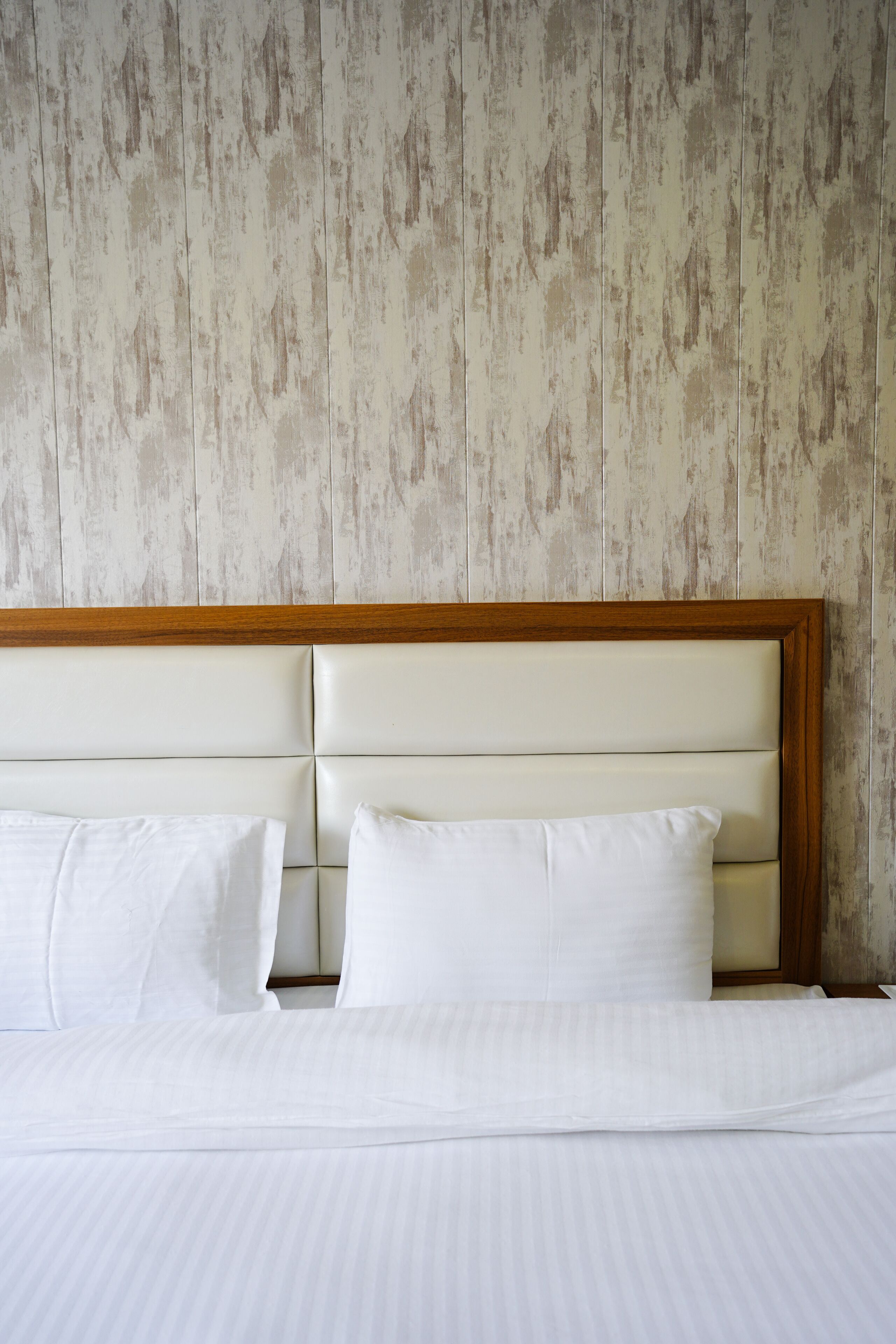 Una cama con sábanas blancas y cabecera de madera frente a una pared con textura.