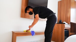 A person cleaning a wooden bench in a room with a flat-screen TV mounted on the wall. - Hotel Northwind Mohali (Kharar)