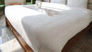 A large bed with a wooden frame, a headboard, and white bedding. There is a green chair and a small round table beside the bed. - Hotel Northwind Mohali (Kharar)