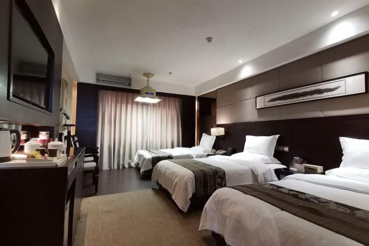 Una camera d'albergo con due letti, una scrivania, una sedia, una lampada e un'ampia finestra con tende.