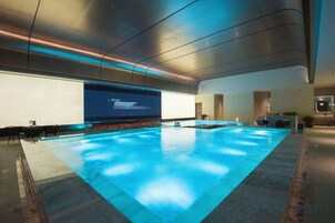 A modern indoor swimming pool with a large screen displaying text, a bar area, and a well-lit space.