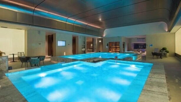 A large indoor swimming pool with a modern design, surrounded by seating areas and a reception desk. - Jinlongtan jiudian (Zhaodong)