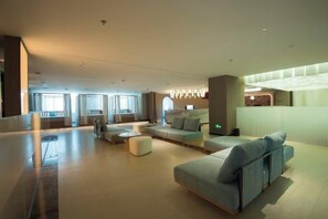 A modern hotel lobby with a seating area, a reception desk, and a large window.