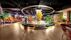 A spacious lobby with a central circular seating area, surrounded by various plants and seating arrangements. - Jinlongtan jiudian (Zhaodong)