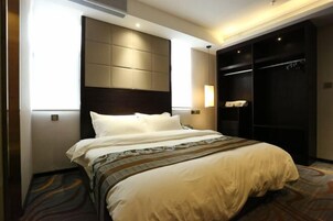 A hotel room with a large bed, a headboard with storage compartments, a wardrobe, and a bedside table with a lamp.