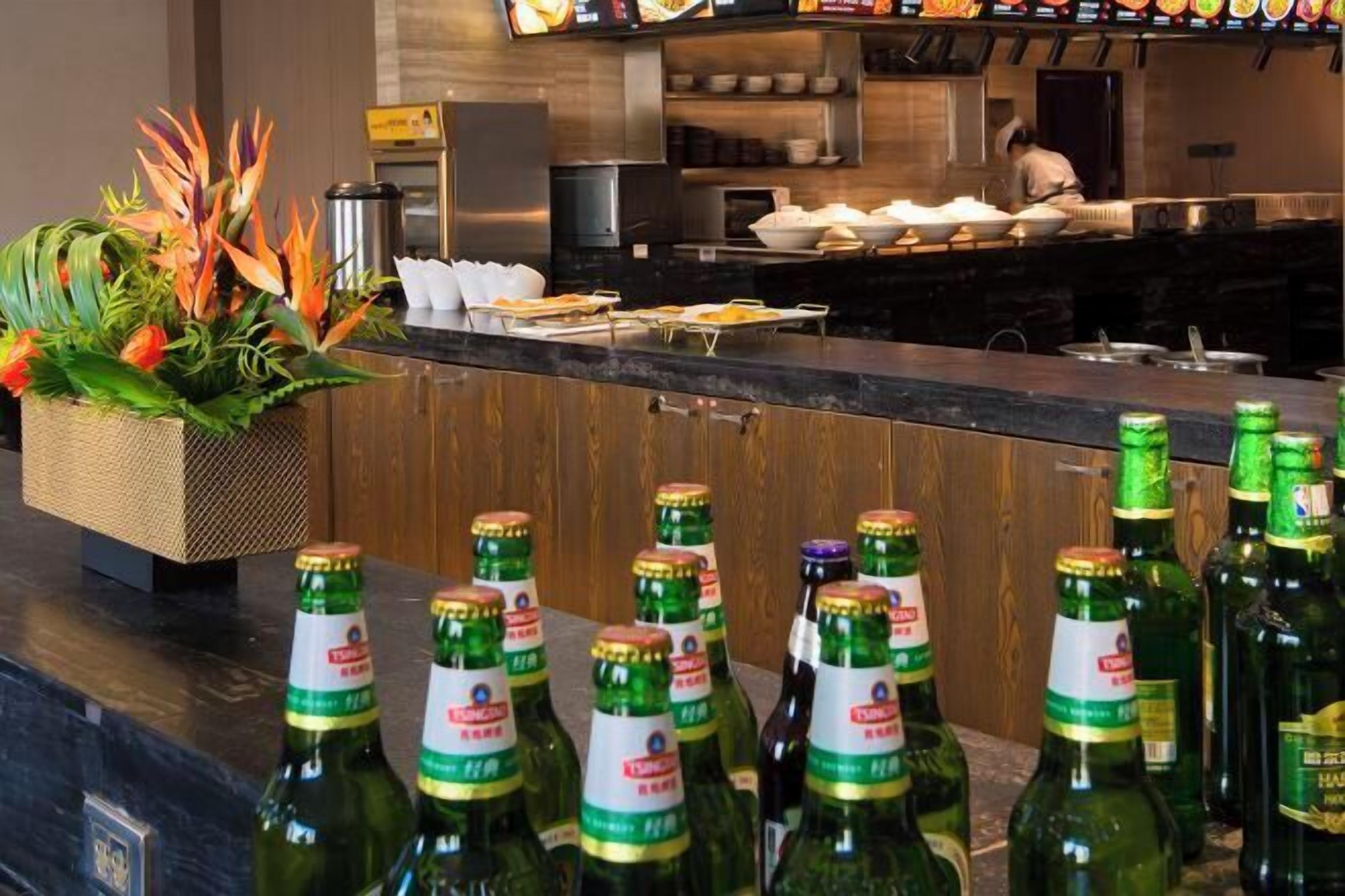 A hotel bar area with bottles of beer, a buffet setup, and a chef preparing food in the background.