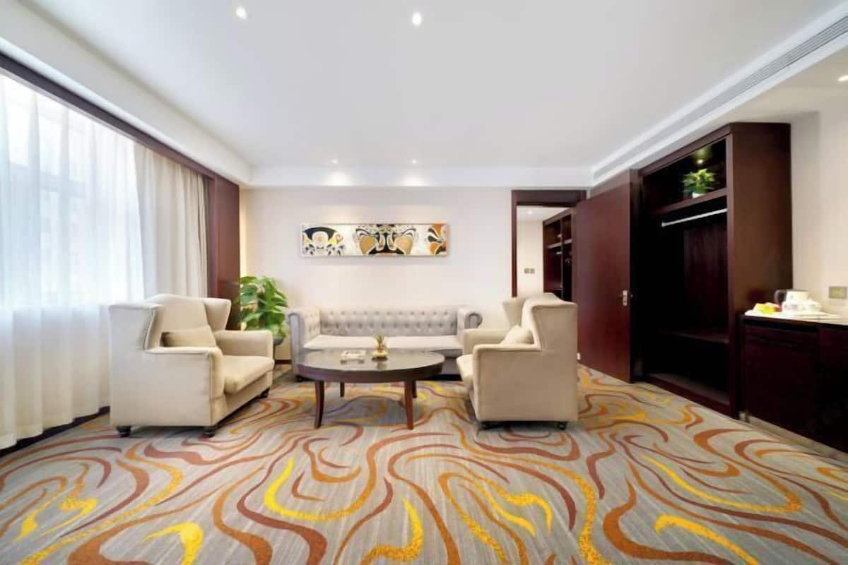 A hotel room with a sofa set, two armchairs, a coffee table, and a patterned carpet.