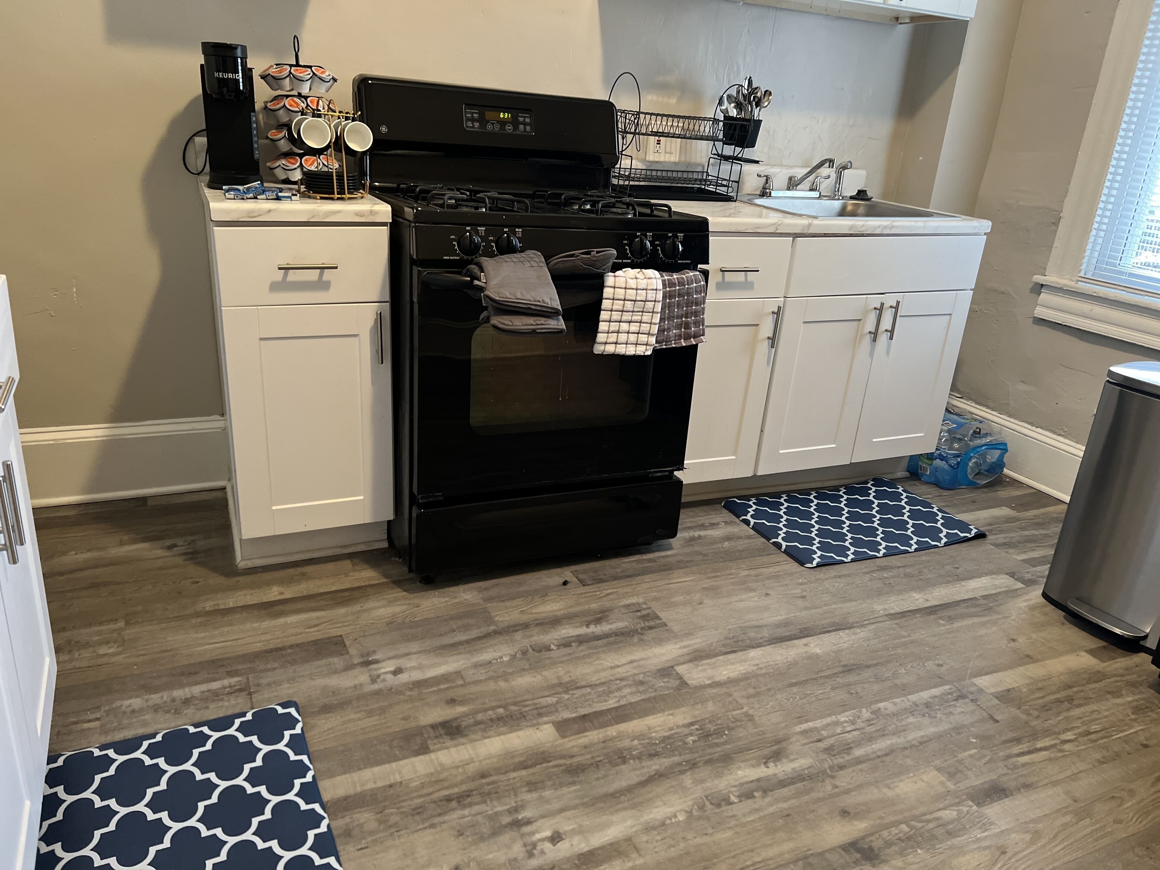 A kitchen with white cabinets, a black stove, a coffee maker, and a sink.