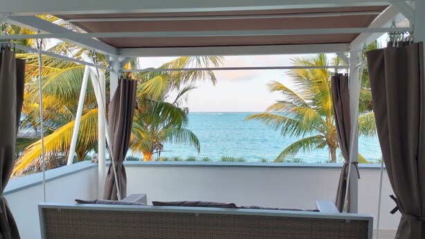 A balcony with a view of the ocean, palm trees, and a bed with a view. - Ahadi Beach Villa, beautifully modern with pool beach access fantastic sea views (Mtwapa)