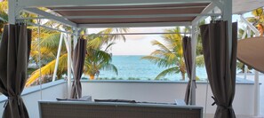 A balcony with a view of the ocean, palm trees, and a bed with a view. - Ahadi Beach Villa, beautifully modern with pool beach access fantastic sea views (Mtwapa)