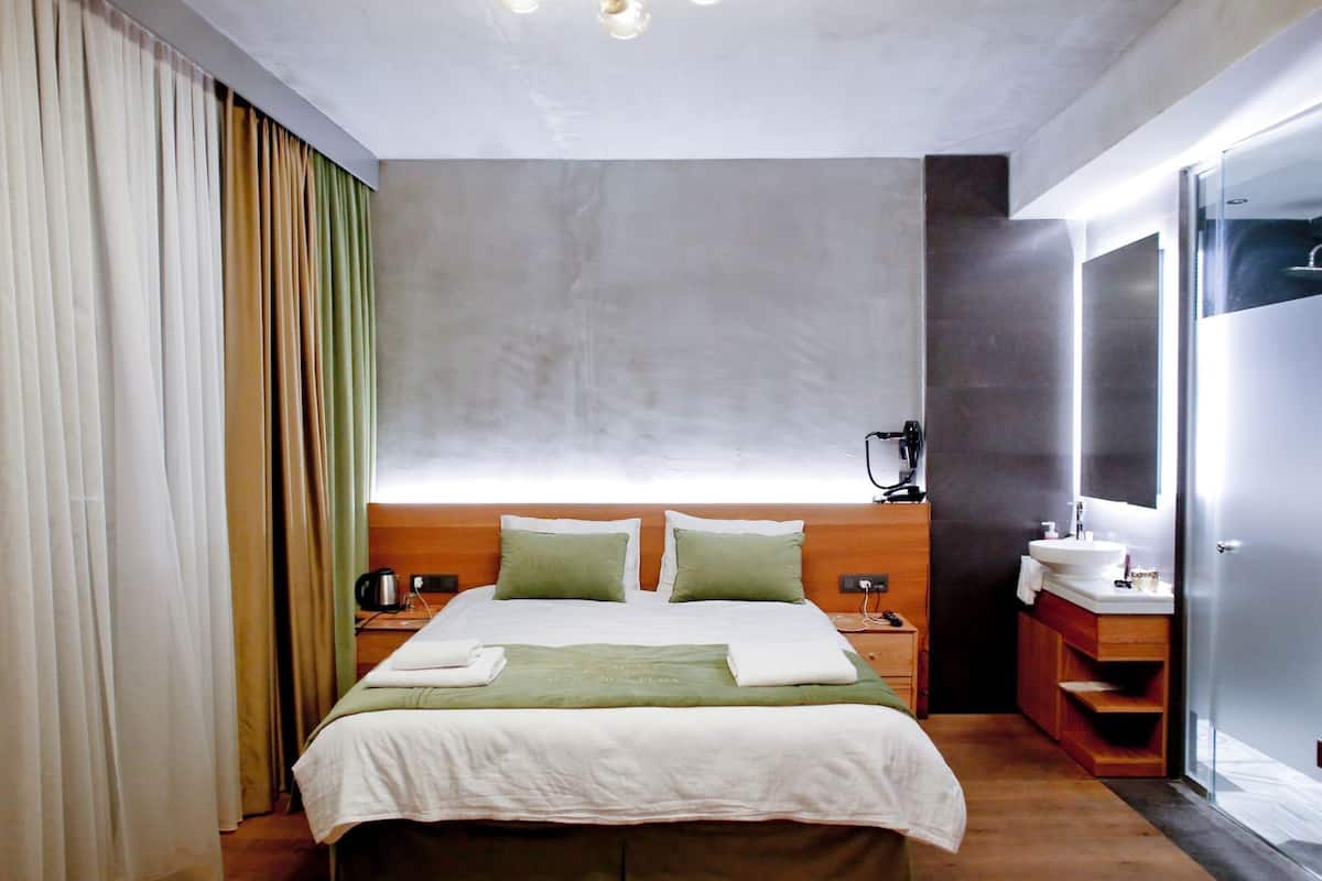 A hotel room with a bed, a nightstand, a vanity with a mirror, and a window with curtains.