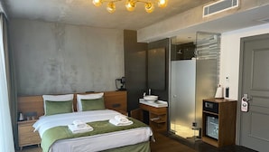 Habitació d'hotel amb llit, taules de nit, un mirall, un bany petit amb un lavabo i un mirall, i una porta amb pom.