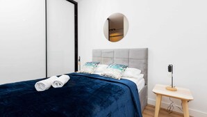 A modern bedroom with a large bed, a bedside table, a mirror, and a wall-mounted light.