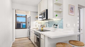 A modern kitchen with white cabinetry, a built-in microwave, and a window with a view. - Breezy condo w/ pool & beach access (Honolulu)