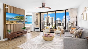 A modern living room with a large TV, a ceiling fan, a sofa, and a view of the city. - Breezy condo w/ pool & beach access (Honolulu)