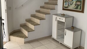 A staircase leading to a landing, a small cabinet with a decorative top, and a painting on the wall. - Cozy townhouse in gated community for families - strategic point in Enseada (Guarujá)