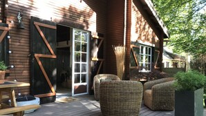 Una terraza de madera con muebles de mimbre, una mesa y plantas en macetas.