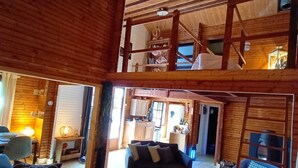 Un amplio espacio tipo loft con techo alto, vigas de madera, un nivel entre pisos y una zona de estar acogedora con sofá y sillones.