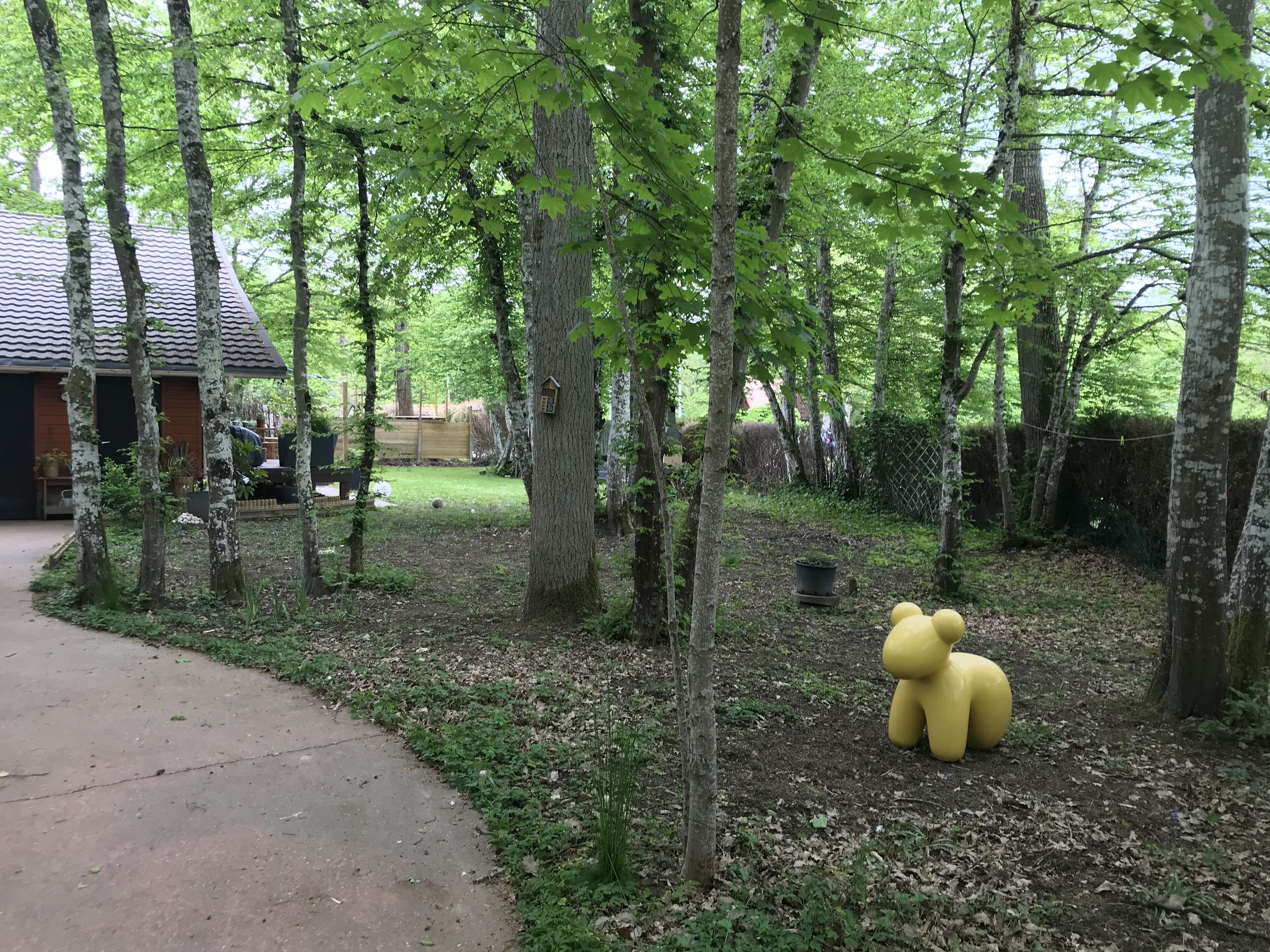 Un espace boisé avec une sculpture d’ours jaune, un chemin pavé et, au fond, un bâtiment doté d’un toit en tuiles.