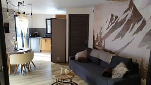 Ein modernes Wohnzimmer mit einem dunkelblauen Sofa, einem runden Couchtisch aus Holz und einem Wandbild mit Bergmotiv.