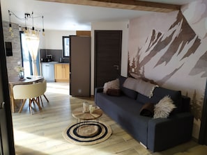 Una sala de estar moderna con un sofá azul oscuro, una mesa de centro redonda de madera y un mural temático de montañas.