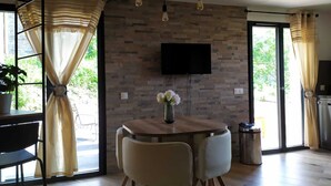 Ein moderner Essbereich mit einem runden Tisch, vier Stühlen, einem an einer Ziegelwand befestigten Fernseher und einem Topf mit Pflanze.