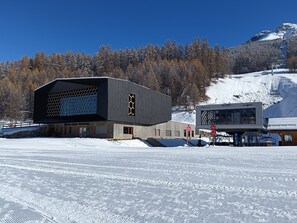 Un bâtiment moderne doté d’une grande façade en verre, avec un télésiège visible en arrière-plan.