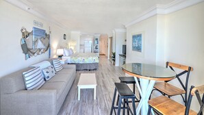 Um espaço compacto com cama, sofá, mesa de jantar com cadeiras e cozinha ao fundo.