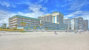 Un hotel sulla spiaggia con diversi piani, balconi e una spiaggia in primo piano.