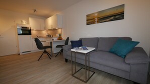 Un salon moderne avec un canapé gris, une table basse et un tableau représentant un coucher de soleil sur l’océan.