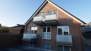 Une maison à deux étages, construite en briques, avec un toit en pente, deux balcons et un petit jardin devant.