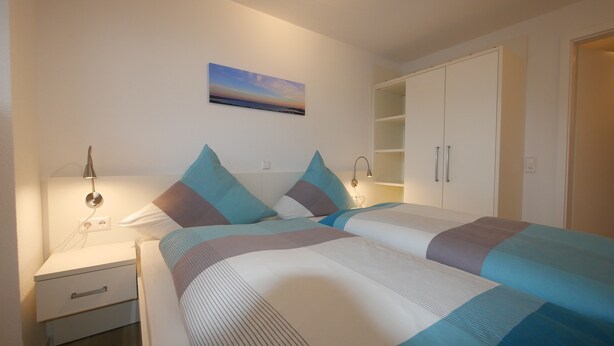 Une chambre à coucher comprenant un lit, des tables de chevet, une commode, une lampe fixée au mur, un tableau et une armoire.