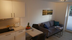 Un espace de vie compact comprenant un coin cuisine, une table à manger, un canapé et un tableau accroché au mur.
