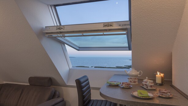 Een knus hoekje met uitzicht op zee, een gedekte tafel met thee en lekkernijen, en een comfortabele stoel.
