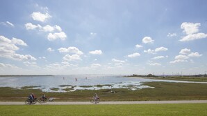 Een kustgebied met een verhard pad, grasvelden en een waterpartij.
