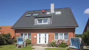 Ein zweistöckiges Haus mit Backsteinfassade, einem Ziegeldach und einer Veranda mit zwei blau gestreiften Stühlen.
