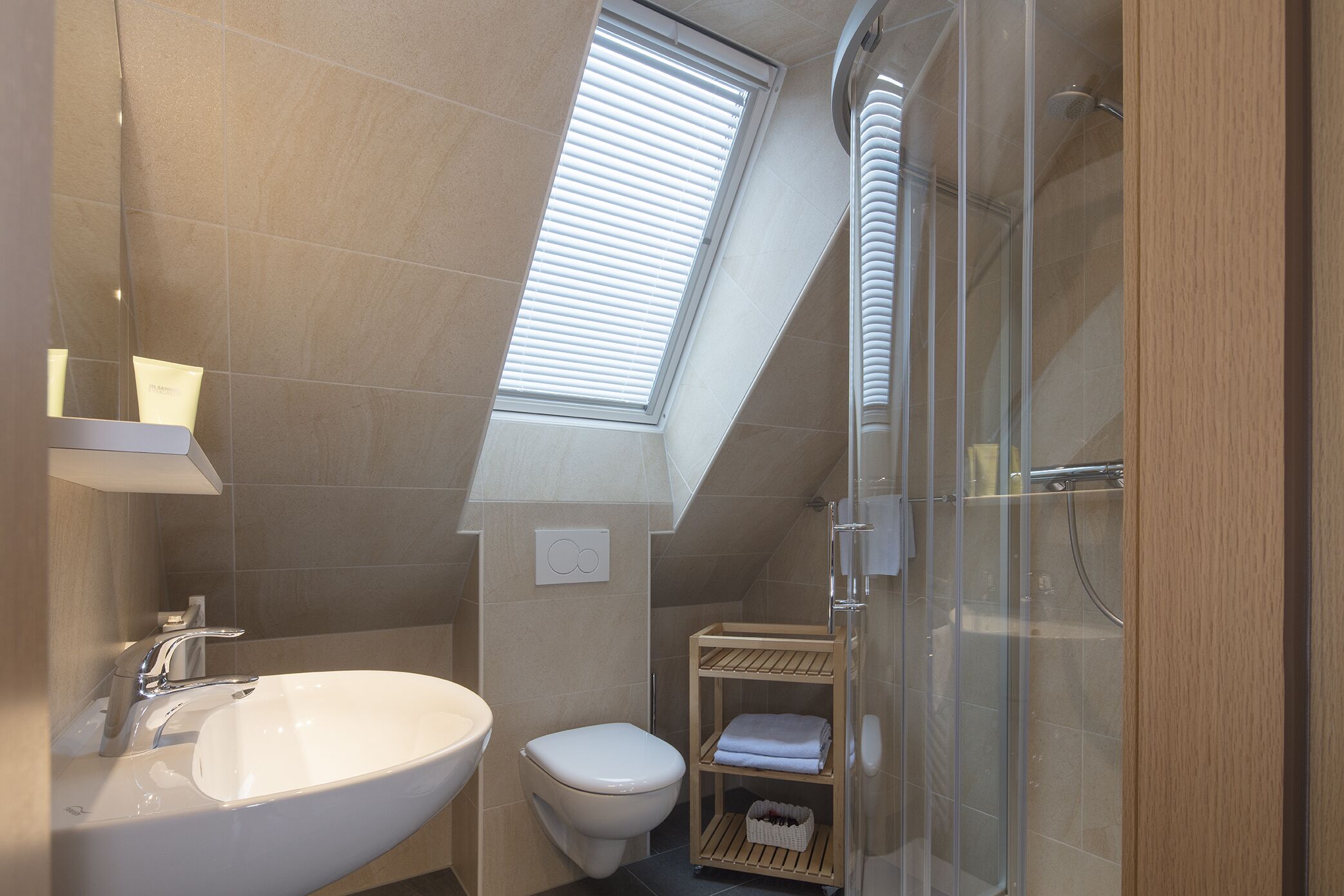 Een moderne badkamer met dakraam, een vrijstaand badkamermeubel, toilet en een douchecabine met glazen wanden.