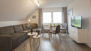 Ett modernt vardagsrum med en soffa, ett matbord, stolar, en tv och ett litet bord med ett ljus.