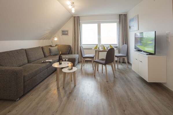 A modern living room with a sofa, a dining table, chairs, a TV, and a small table with a candle.