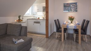 Una cocina moderna con armarios blancos, una mesa de comedor de madera con cuatro sillas y una zona de comedor con un jarrón de flores.