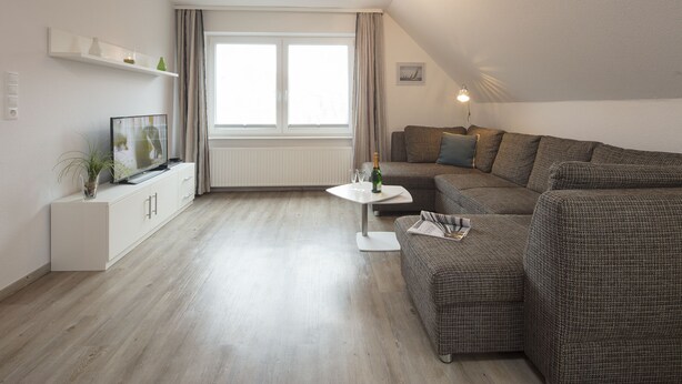 Una sala moderna con un sofá modular, una mesita blanca y un televisor sobre un mueble.