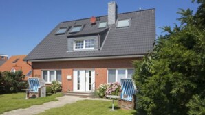 Una casa de dos pisos con techo inclinado, chimenea y un pequeño porche delantero.